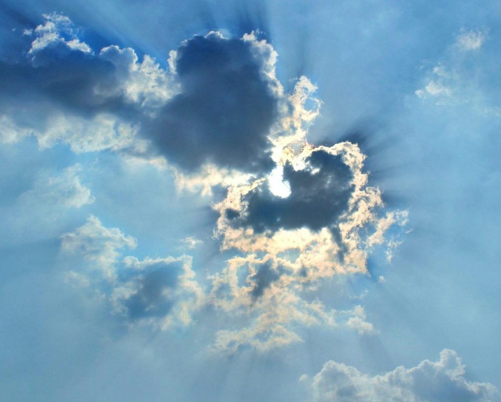 The sun is shining through the clouds in the sky