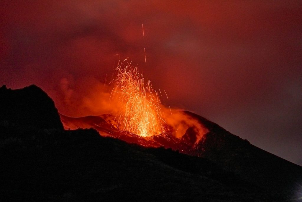 Bright orange lava erupting from a dark volcanic mountain at night