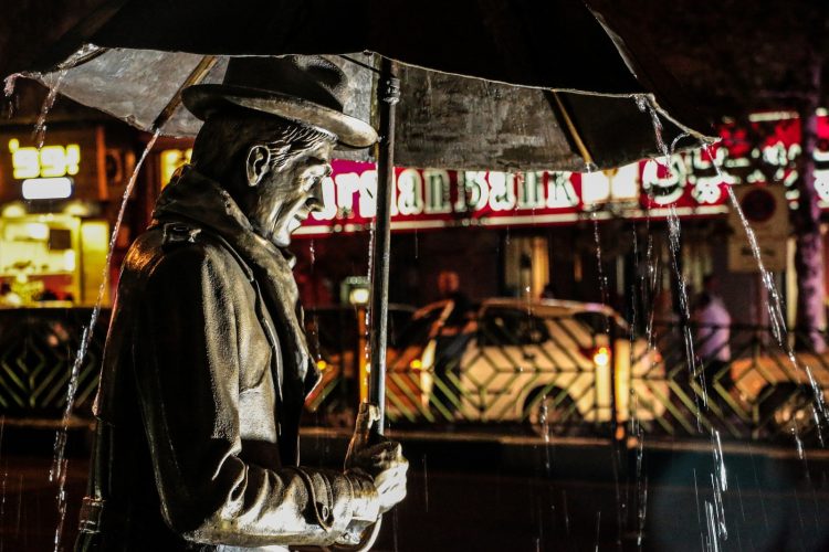 shallow focus photography of man carrying umbrella statue