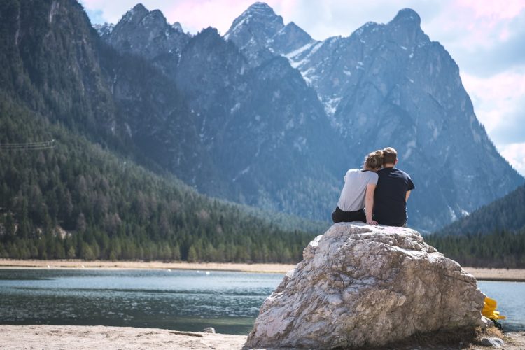 a couple sits on a rock looking out over a lake