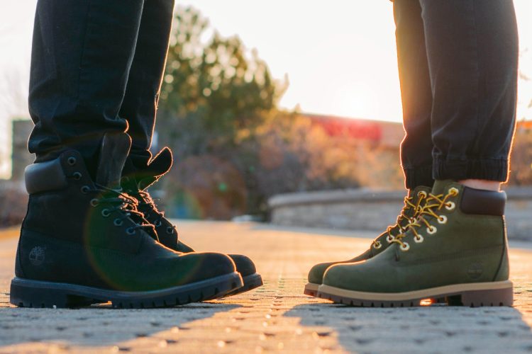two people wearing green-and-black work boots standing on gray concrete pavement