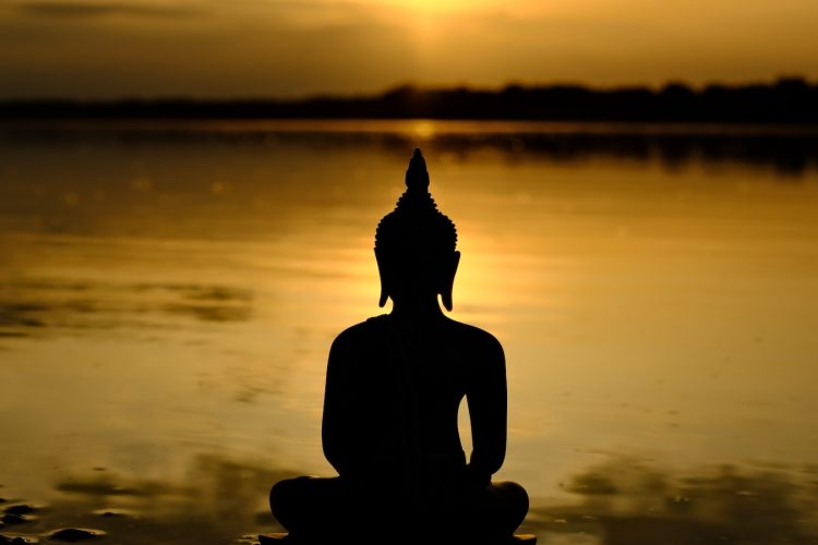 a buddha statue sitting in front of a body of water