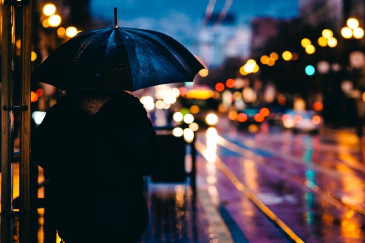 person walking on street while holding black umbrella near cars on road at nighttime