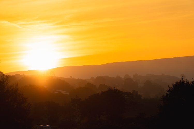 the sun is setting over the hills and trees